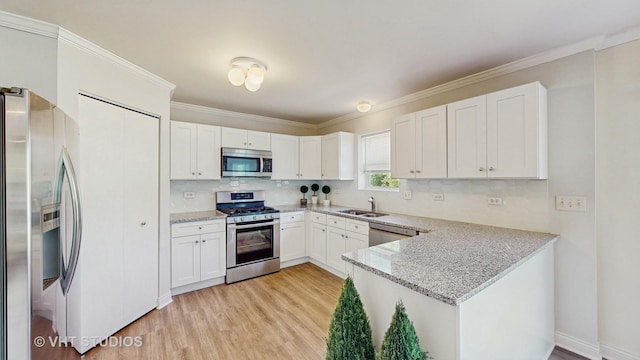 kitchen featuring appliances with stainless steel finishes, a sink, light wood finished floors, a peninsula, and white cabinetry