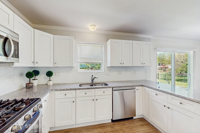 kitchen featuring stainless steel appliances, a sink, ornamental molding, white cabinets, and backsplash