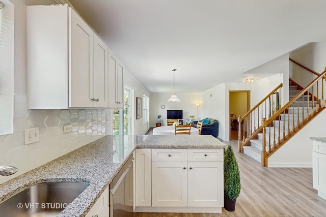 kitchen featuring a sink, a peninsula, light wood finished floors, tasteful backsplash, and white cabinets