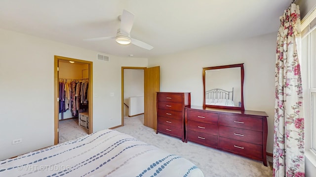 bedroom featuring a walk in closet, light colored carpet, a ceiling fan, and a closet