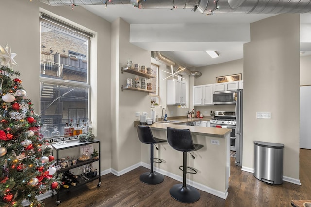 kitchen featuring appliances with stainless steel finishes, a sink, dark wood-style flooring, white cabinets, and a peninsula