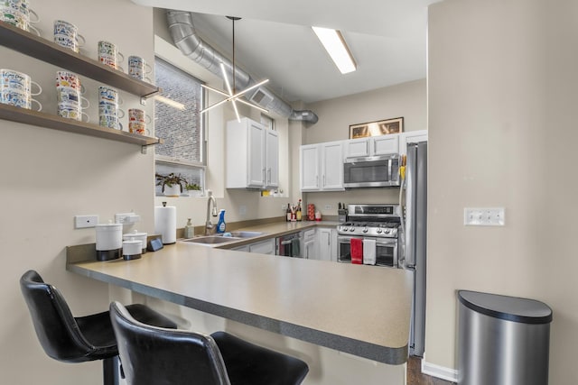 kitchen with appliances with stainless steel finishes, a sink, a peninsula, a kitchen bar, and white cabinets