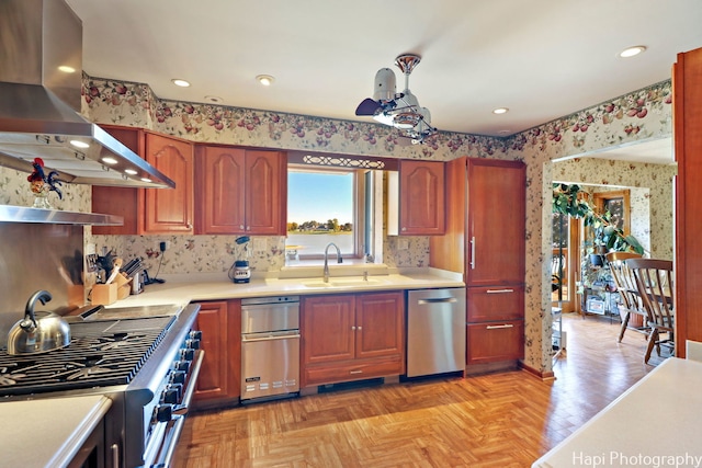 kitchen featuring stainless steel appliances, wall chimney range hood, a sink, wallpapered walls, and light countertops