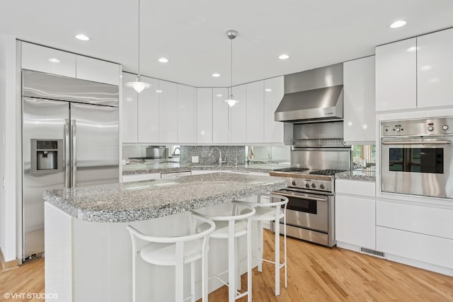 kitchen with stainless steel appliances, modern cabinets, wall chimney exhaust hood, white cabinetry, and recessed lighting