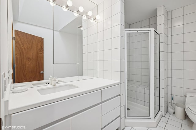 bathroom with a stall shower, toilet, tile patterned floors, vanity, and tile walls