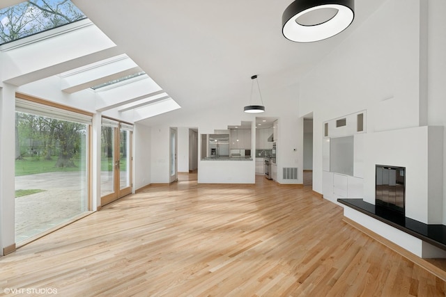 unfurnished living room featuring a skylight, light wood-style floors, a glass covered fireplace, baseboards, and high vaulted ceiling