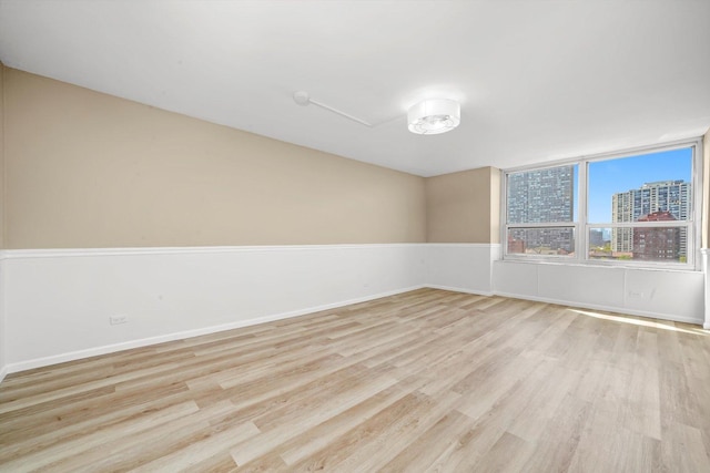 unfurnished room featuring light wood-style floors, a city view, and baseboards
