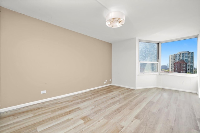 spare room with light wood finished floors, baseboards, and a view of city