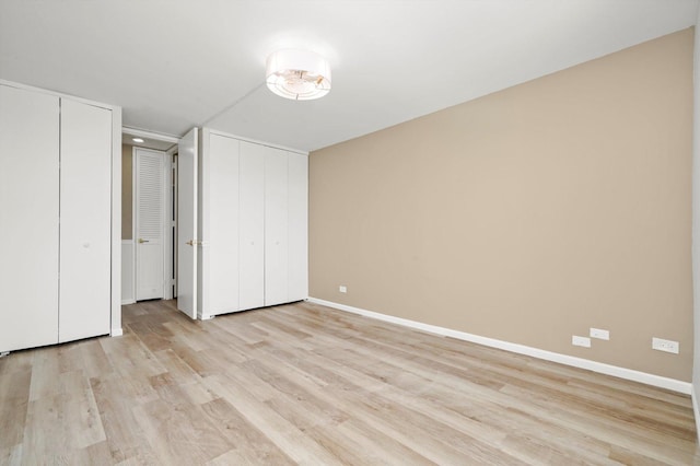 unfurnished bedroom with light wood-type flooring, multiple closets, and baseboards