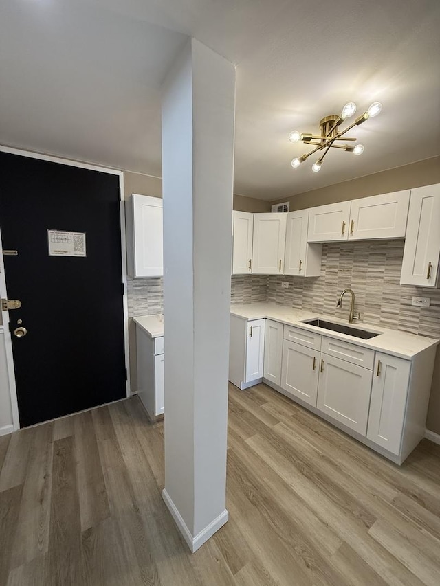 kitchen featuring a sink, backsplash, white cabinets, and light countertops