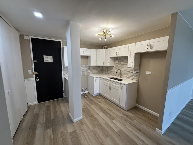 kitchen with a sink, a chandelier, light wood-style flooring, tasteful backsplash, and white cabinetry