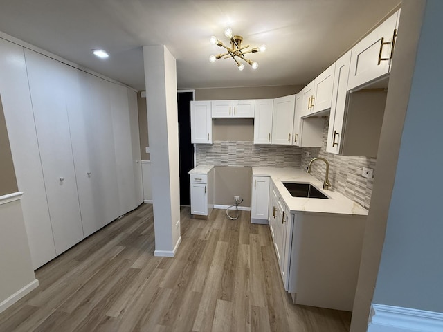 kitchen with a sink, a chandelier, decorative backsplash, light wood finished floors, and white cabinetry