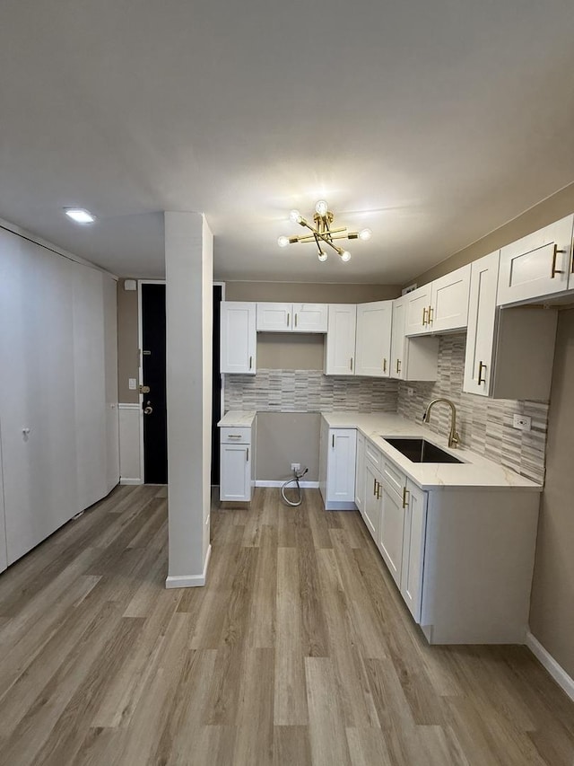 kitchen featuring a sink, decorative backsplash, light wood-type flooring, white cabinetry, and a chandelier