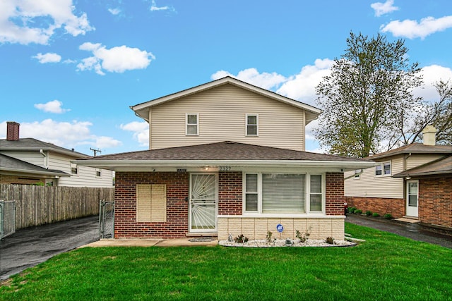 view of front of property featuring brick siding, fence, and a front lawn