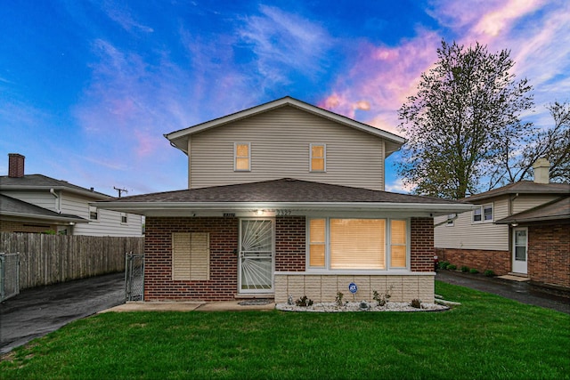 back of property featuring fence, a lawn, and brick siding