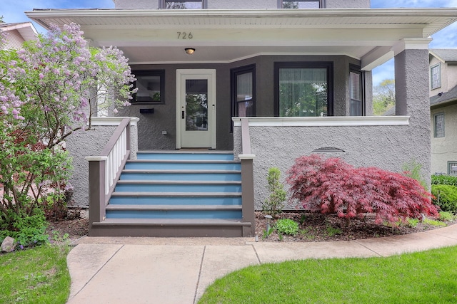 view of exterior entry with covered porch and stucco siding