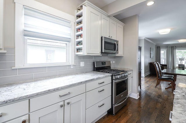 kitchen featuring appliances with stainless steel finishes, white cabinetry, backsplash, dark wood finished floors, and ornamental molding