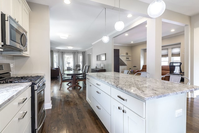 kitchen with appliances with stainless steel finishes, ornamental molding, a center island, light stone counters, and dark wood-style floors