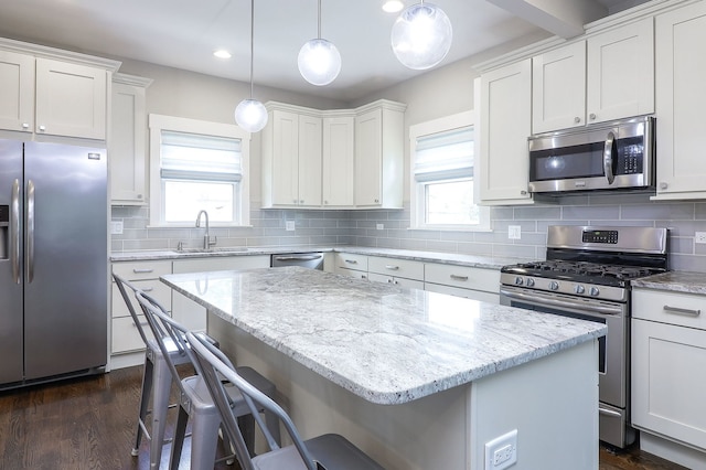kitchen with appliances with stainless steel finishes, a sink, a center island, a kitchen bar, and white cabinetry
