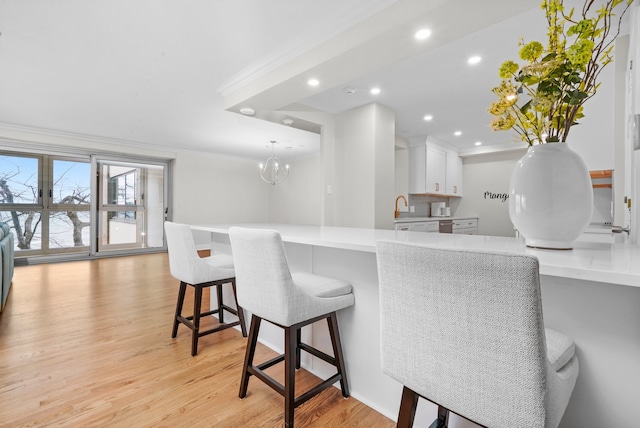 kitchen featuring a kitchen breakfast bar, crown molding, white cabinetry, light countertops, and light wood-style flooring