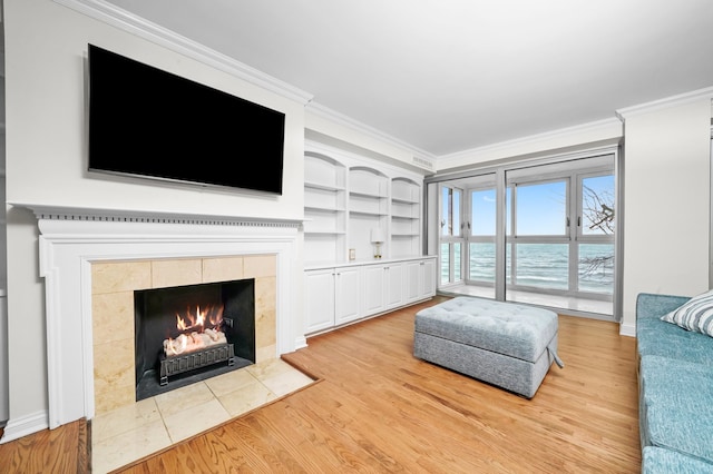 living room featuring a tiled fireplace, ornamental molding, and light wood-style flooring