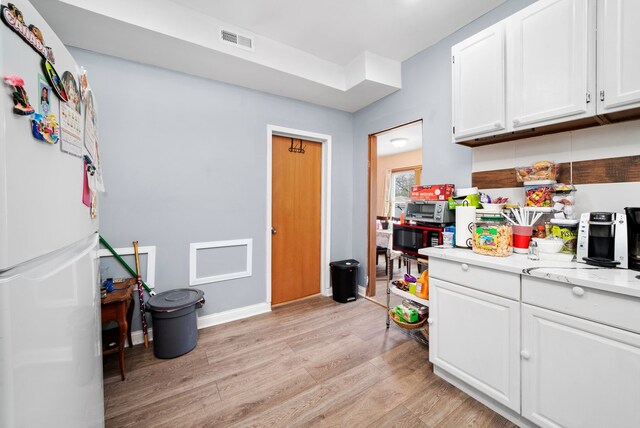 kitchen with visible vents, freestanding refrigerator, baseboards, light wood-type flooring, and white cabinets