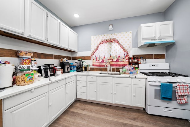 kitchen featuring a sink, under cabinet range hood, white cabinets, and white gas range