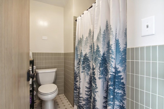 full bath with toilet, a shower with curtain, tile walls, and a wainscoted wall