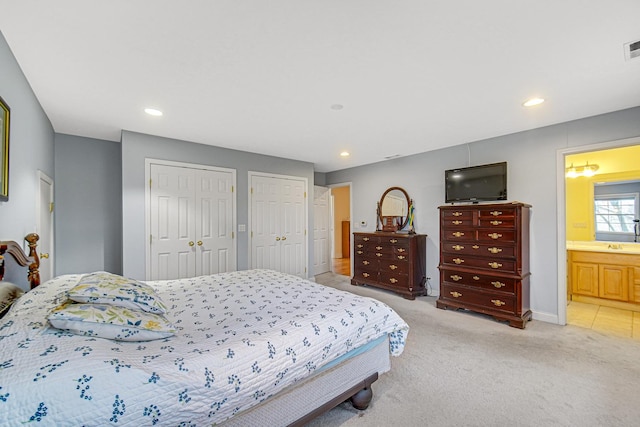 bedroom with visible vents, multiple closets, ensuite bathroom, light carpet, and recessed lighting