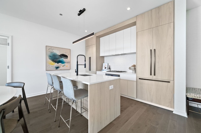 kitchen with a sink, light countertops, dark wood-type flooring, a center island with sink, and modern cabinets