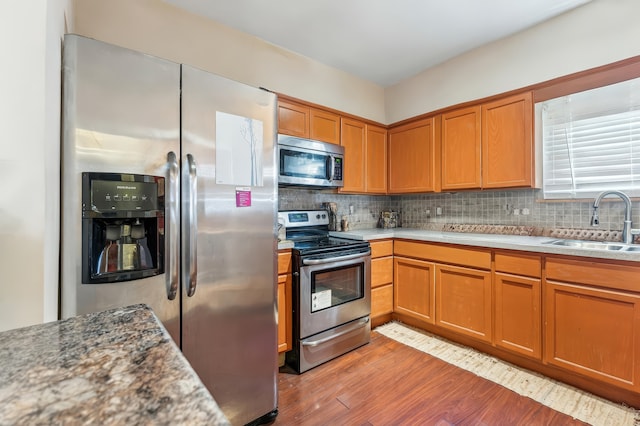 kitchen featuring brown cabinets, appliances with stainless steel finishes, a sink, light wood finished floors, and backsplash