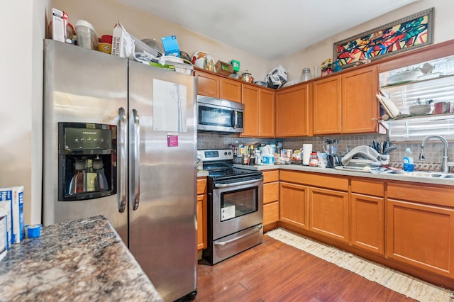 kitchen with brown cabinetry, light wood-type flooring, a sink, appliances with stainless steel finishes, and backsplash
