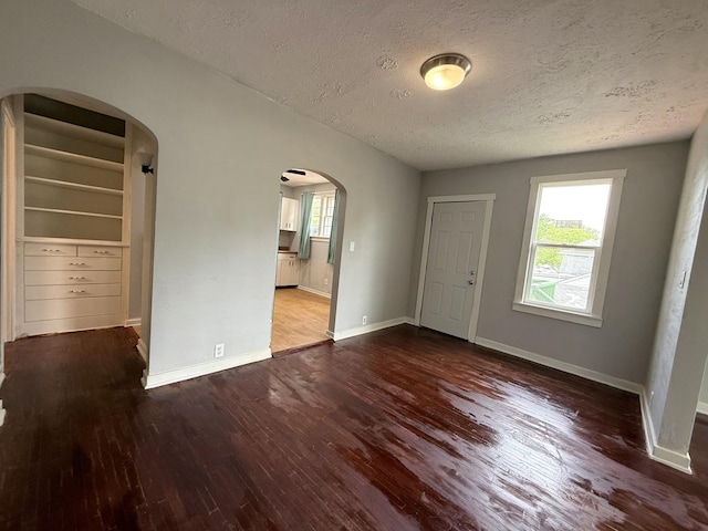 interior space with arched walkways, a textured ceiling, and wood finished floors