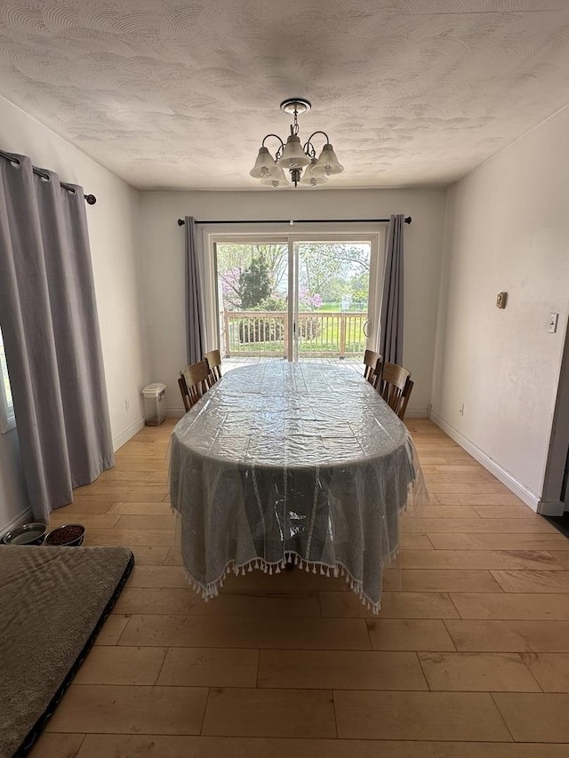 dining space featuring an inviting chandelier, baseboards, light wood finished floors, and a textured ceiling