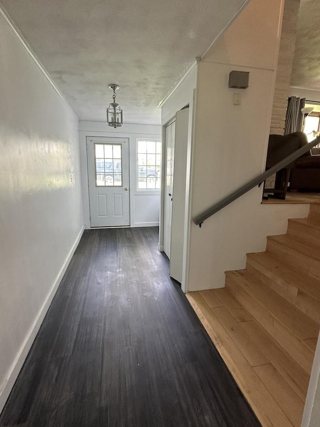 doorway featuring ornamental molding, baseboards, dark wood-style floors, stairway, and a chandelier