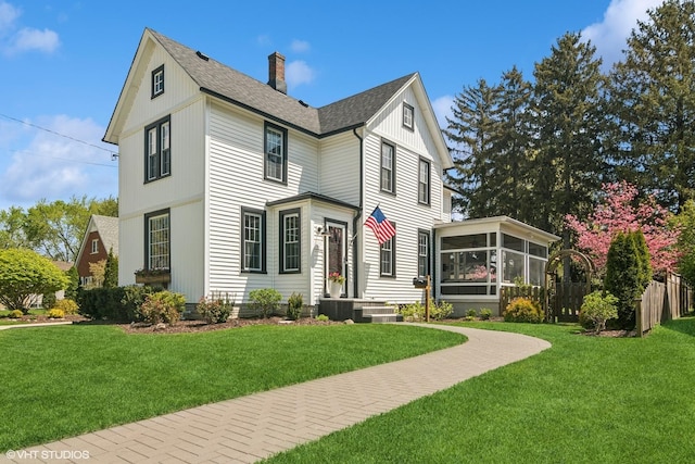 view of front of property featuring a sunroom, a chimney, a shingled roof, and central AC