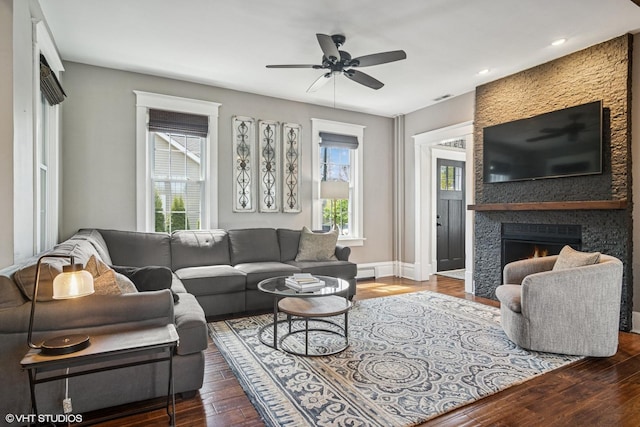 living area with wood finished floors, a fireplace, a ceiling fan, a baseboard heating unit, and baseboards