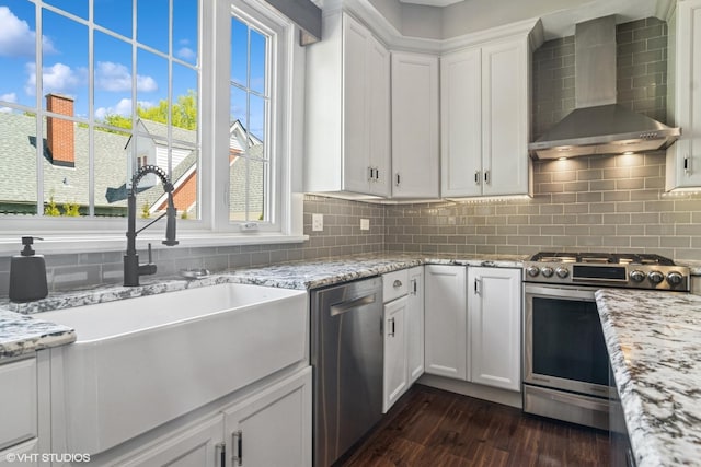 kitchen with stainless steel appliances, wall chimney exhaust hood, a sink, dark wood-style floors, and backsplash