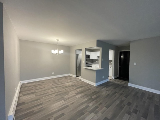 unfurnished living room with dark wood-type flooring, baseboards, and a chandelier