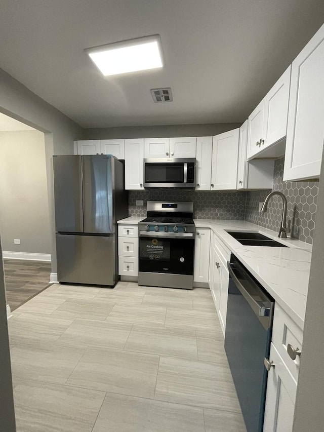 kitchen with white cabinets, stainless steel appliances, a sink, and tasteful backsplash
