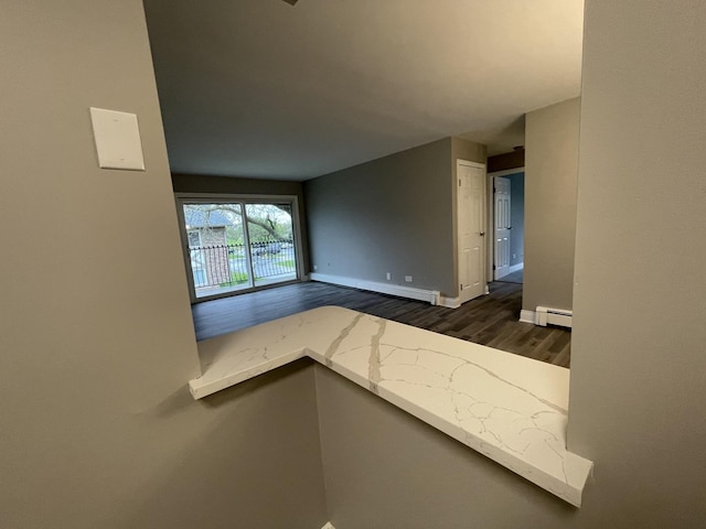empty room featuring baseboards, a baseboard heating unit, and dark wood-type flooring