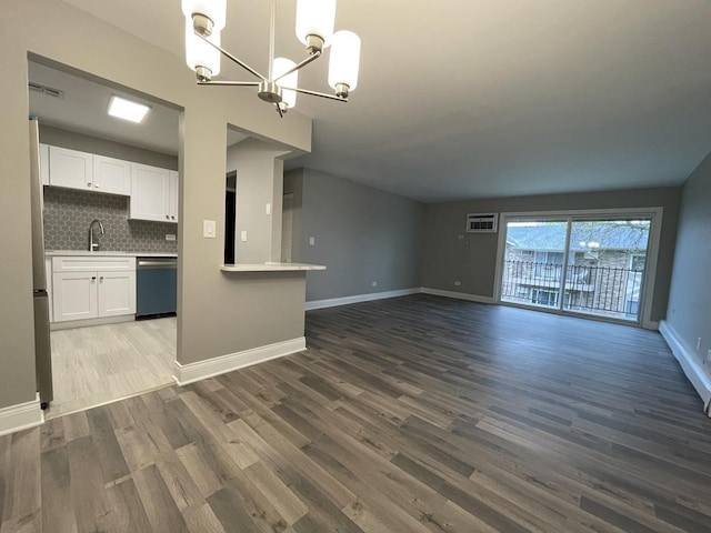 unfurnished living room with a sink, a chandelier, baseboards, wood finished floors, and visible vents