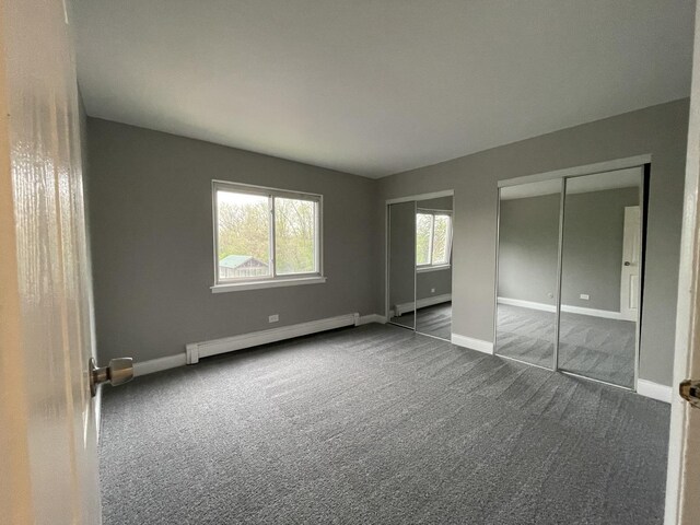 unfurnished bedroom with baseboards, a baseboard radiator, two closets, and carpet flooring
