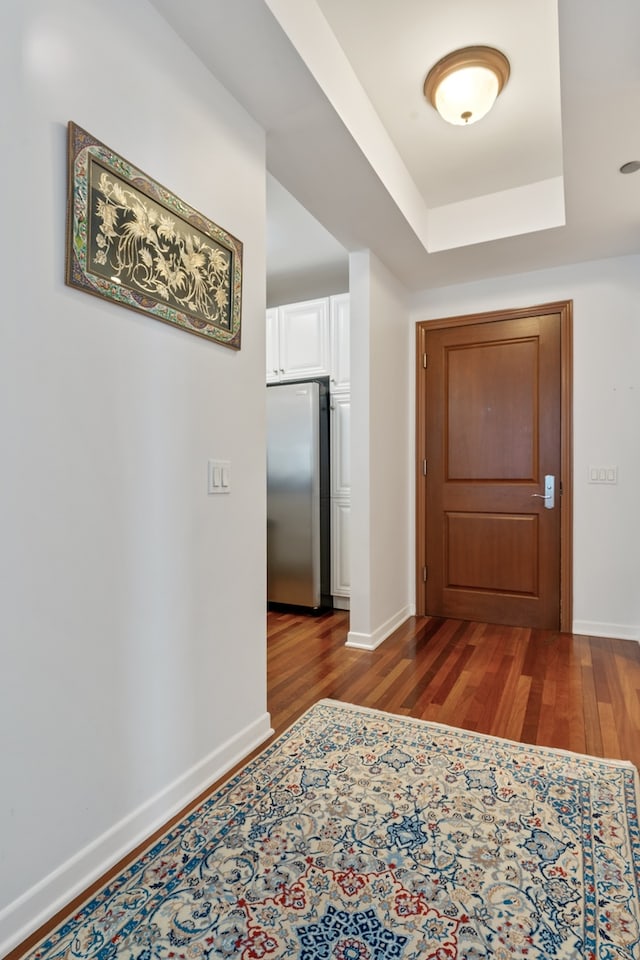 hallway featuring baseboards, dark wood-style floors, and a tray ceiling