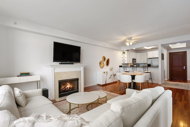 living area with baseboards, a ceiling fan, wood finished floors, and a tile fireplace