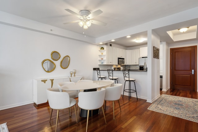 dining area featuring baseboards, dark wood finished floors, ceiling fan, and a tray ceiling