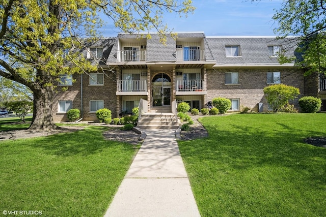 multi unit property featuring mansard roof, brick siding, a shingled roof, and a front yard