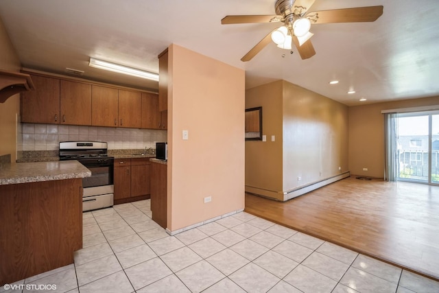 kitchen featuring stainless steel gas stove, light tile patterned flooring, a baseboard radiator, decorative backsplash, and a sink