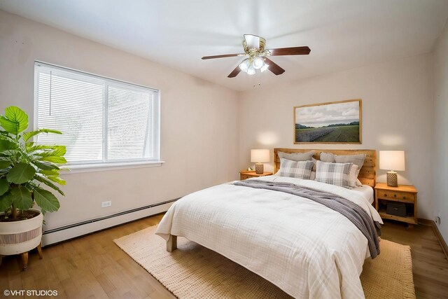bedroom with a baseboard heating unit, wood finished floors, baseboards, and a ceiling fan