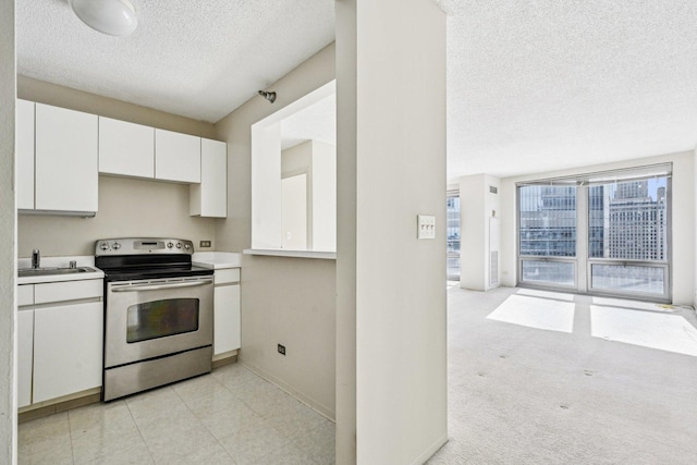 kitchen featuring a textured ceiling, stainless steel electric range, a sink, light countertops, and white cabinetry